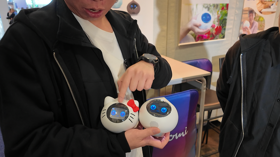 A man holds two baby robots with faces on them.