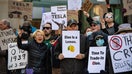 Protesters hold signs during a protest against Elon Musk and his Tesla car company outside the Tesla dealership in Boston, Mass. on March 15, 2025. 