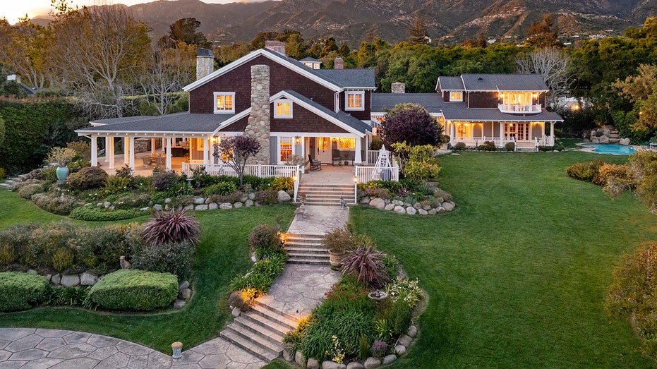 A stone walkway with some stairs, lined with grass on either side, leads to the home's front porch.