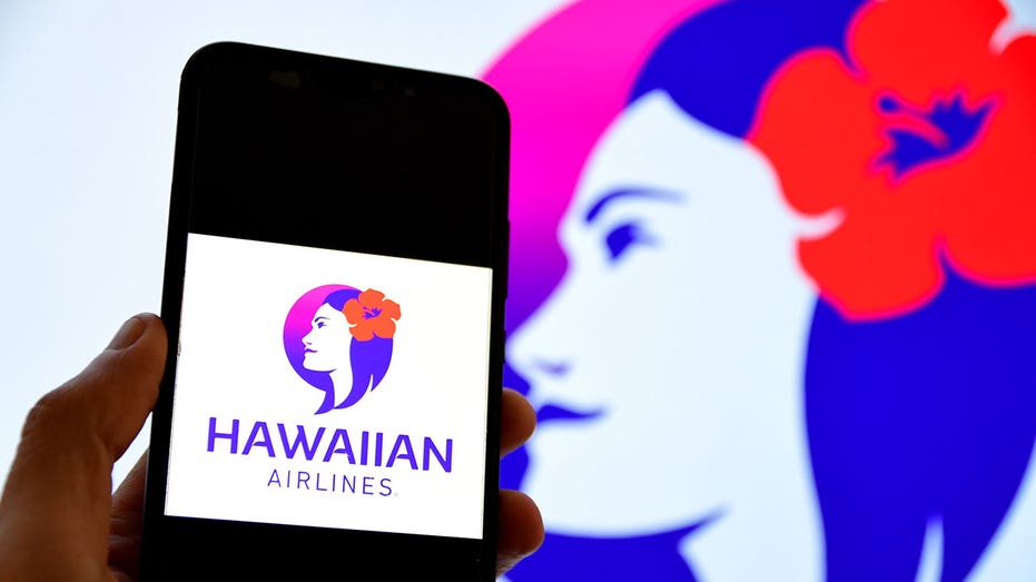 FRANCE - 2025/03/07: In this photo illustration, Hawaiian Airlines Company is seen displayed on a smartphone screen with the logo displayed in the background. (Photo Illustration by Romain Doucelin/SOPA Images/LightRocket via Getty Images)