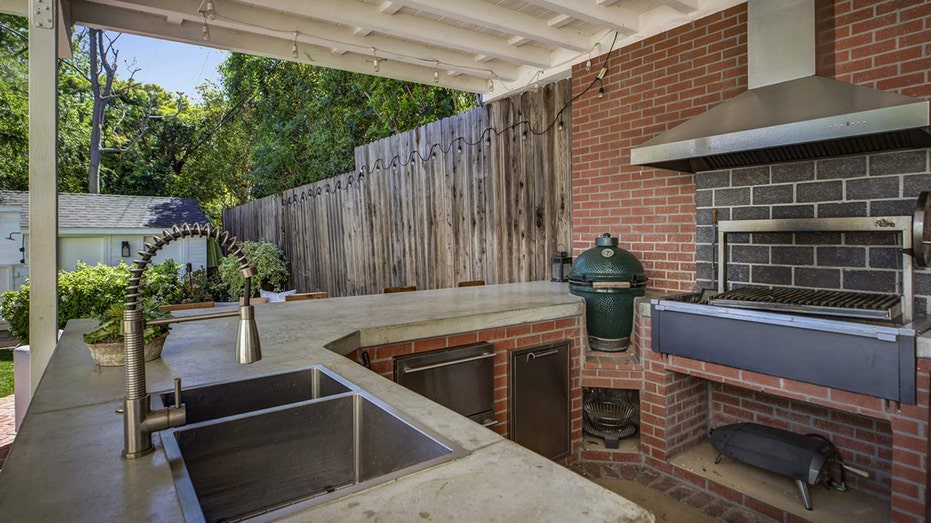 The backyard also features an outdoor kitchen with a barbecue and bar seating.