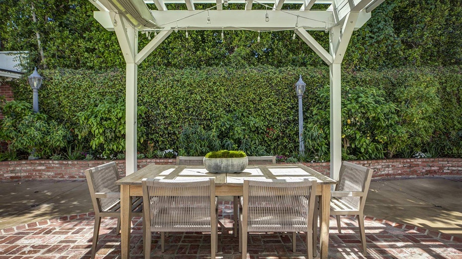 The backyard features an outdoor dining area under a white patio.