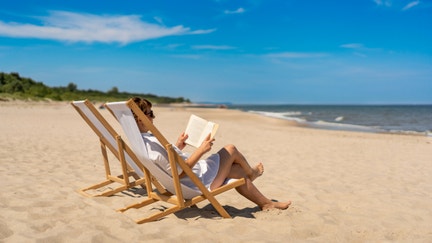 A woman reads a book on a beach. - Fox Business News