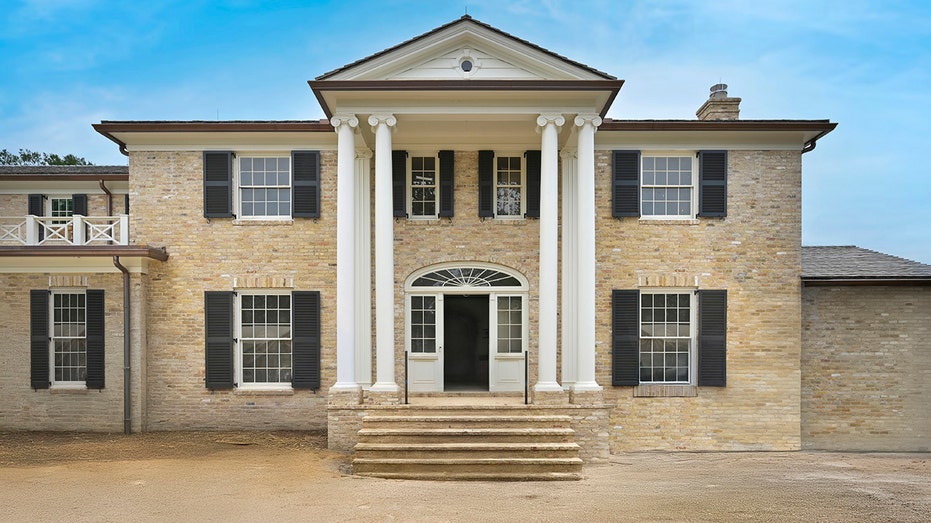 The tan brick home also includes black shutters and a stone staircase leading to the front door.