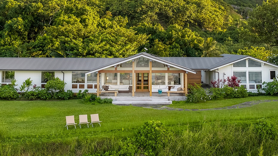 The covered lanai features an outdoor seating area with a grass field in front of it.