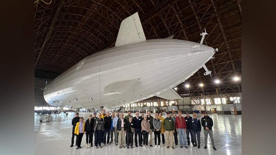Group photo of students and John J. Geoghegan in front of the massive Pathfinder 1 airship inside an air hangar