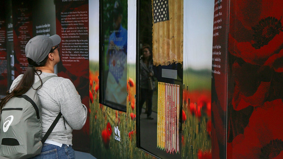 Woman wearing backpack looks at a Memorial Day exhibit with an American flag and poppies inside the Poppy Wall of Honor