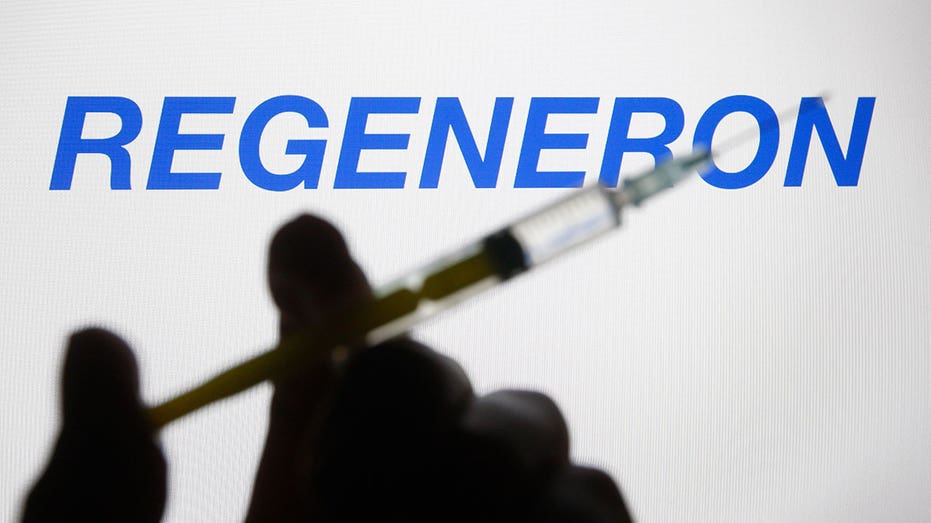 UKRAINE - 2021/02/27: In this photo illustration a Regeneron Pharmaceuticals logo of a US biotechnology company is seen behind a silhouette hand holding a medical syringe. (Photo Illustration by Pavlo Gonchar/SOPA Images/LightRocket via Getty Images)