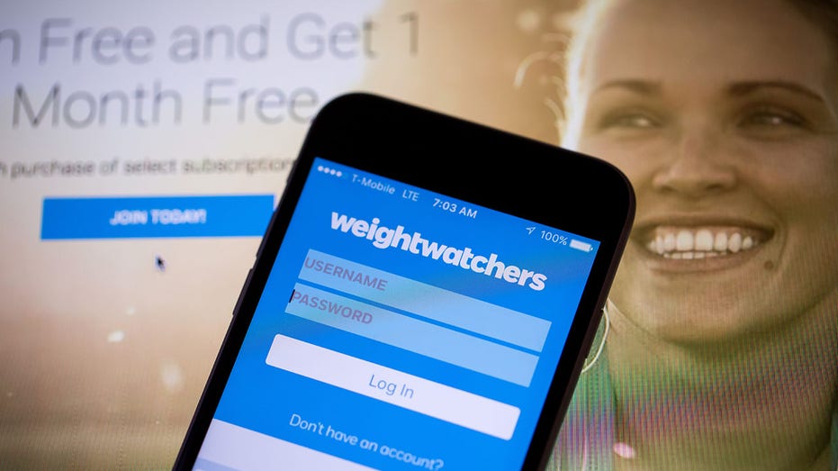 Cellphone with WeightWatchers login in page on it with a Weight Watchers advertisement in the background