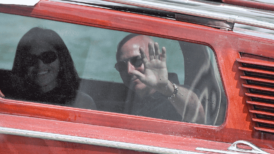 TOPSHOT - Amazon's founder Jeff Bezos and Lauren Sanchez wave from the taxi-boat as they arrive at the Aman Hotel on June 25, 2026. Celebrities in superyachts sail into Venice this week for the three-day wedding party of Amazon tycoon Jeff Bezos and Lauren Sanchez, despite irate locals who say the UNESCO city is no billionaire's playground. The tech magnate and journalist have reportedly invited about 200 guests to their multi-million dollar nuptials in the Italian city, which are expected to kick off on June 26 and end Saturday with a ceremony at a secret location. (Photo by MARCO SABADIN / AFP) (Photo by MARCO SABADIN/AFP via Getty Images)