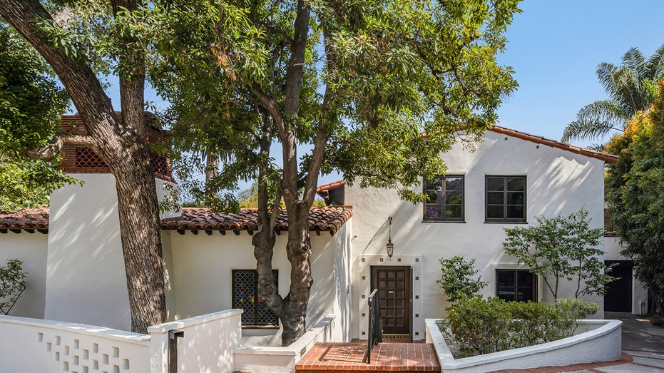 The home features tall trees and a brick walkway leading to the front door.