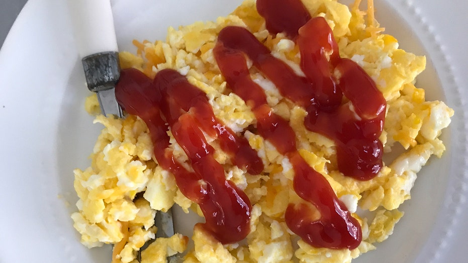 Ketchup spreads scrambled eggs on a white plate.