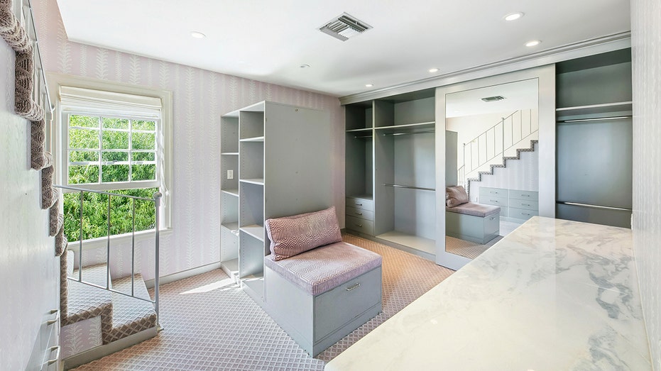 The walk-in closet features built-in shelves and pink wallpaper.
