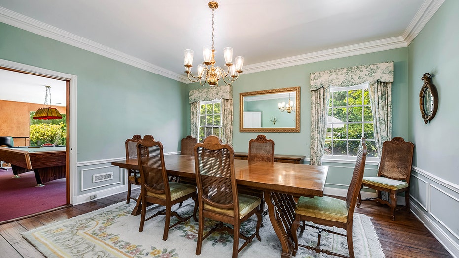 The dining room features green walls with white wainscotting on the lower third and two windows.