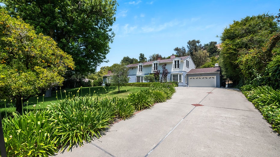 A long driveway leads to the four-car garage, and features a manicured lawn to the left of it.