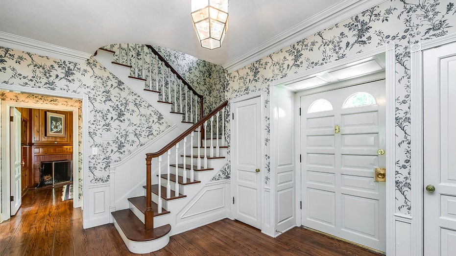 The entryway features wallpaper with navy blue designs, as well as hardwood floors and a staircase leading upstairs.