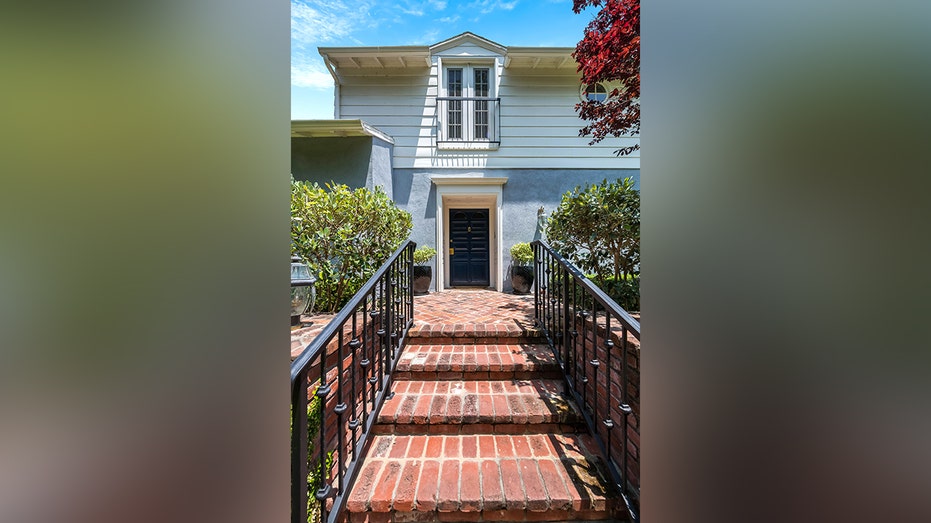 A set of brick stairs leads to the front door of the blue and white wood-paneled home.