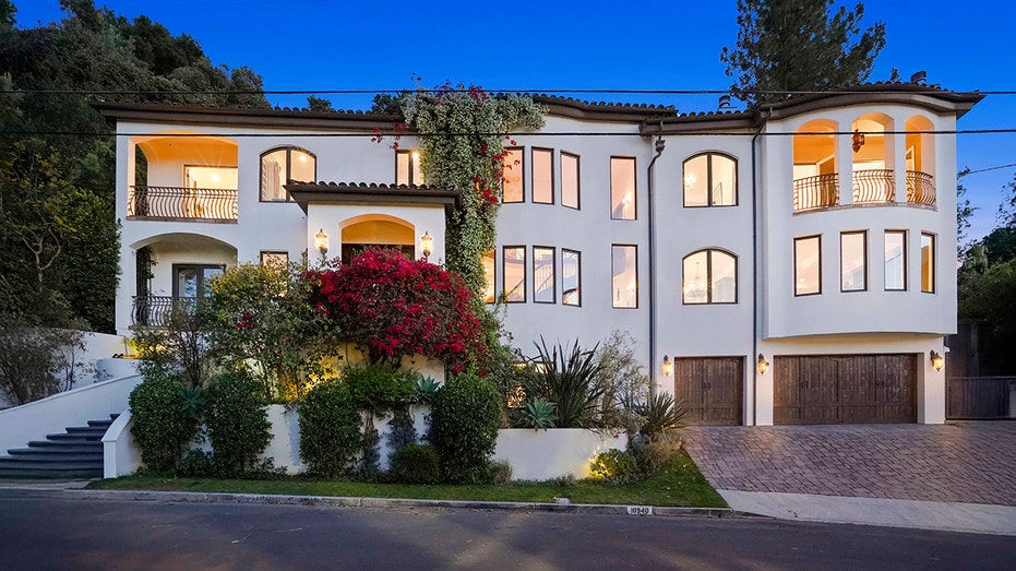 The front of the home is accented with green hedges and a large bush with dark red flowers.