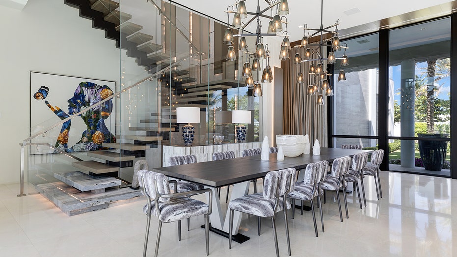 A black dining table with a staircase behind it and light fixtures.