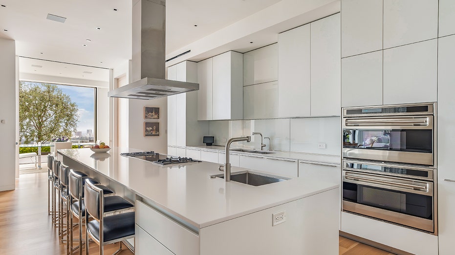 The all-white kitchen features two ovens and an eat-in center island.