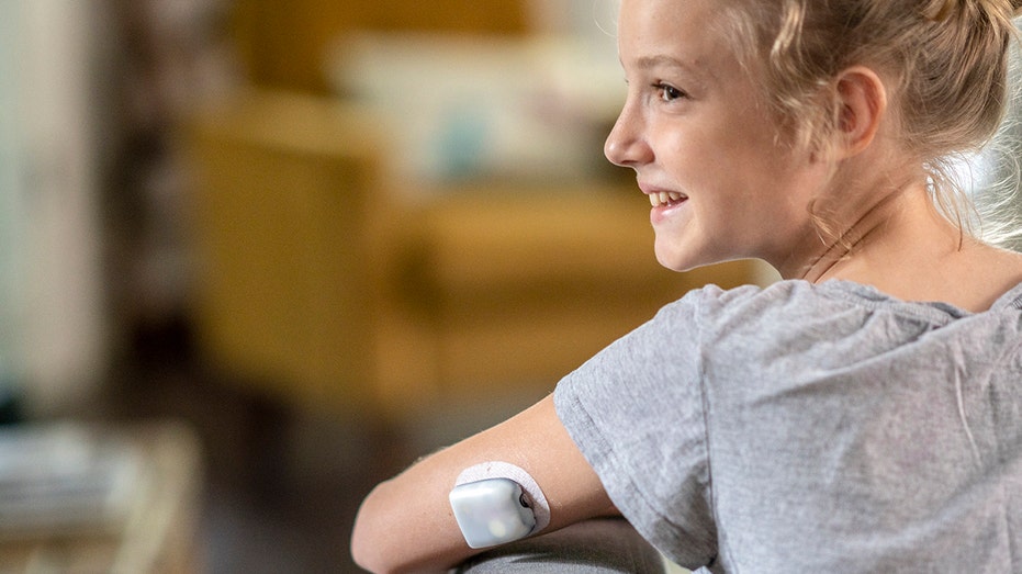 girl with Diabetes sits on couch with CGM on her arm