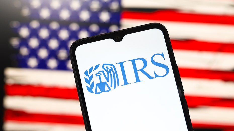 IRS logo on phone screen with US flag on computer screen in background
