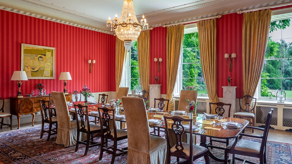 The dining room boasts walls with red wallpaper and a large table in the center.