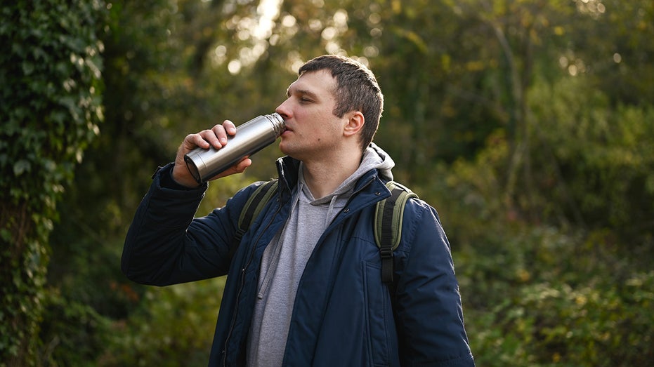 A man is drinking out of a stainless steal water bottle.