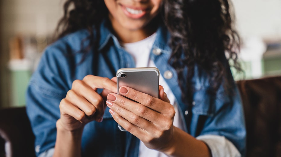 Cropped shot of a young woman using smart phone at home. Smiling african american woman using smartphone at home, messaging or browsing social networks while relaxing on couch