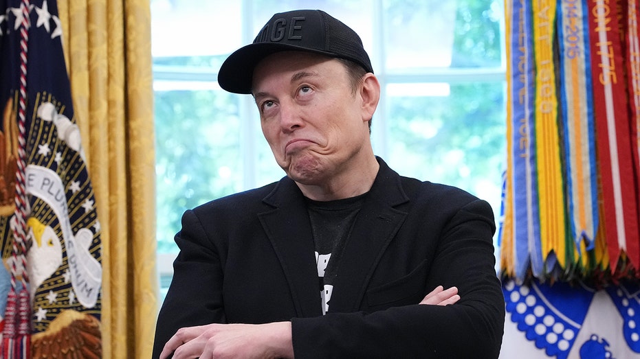 Elon Musk scowling with his arms crossed in the Oval Office