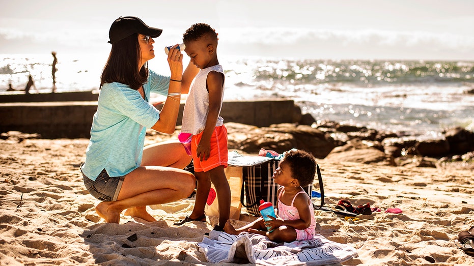 Mom putting suntan lotion on her little children at the beach