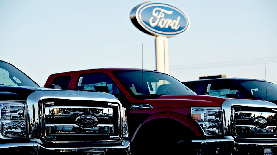 A Ford Motor Co. logo stands behind a row of F-250 pickup trucks at the Rob Baker Ford dealership in Plainfield, Illinois.