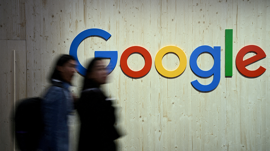 People walk next to a Google logo during a trade fair