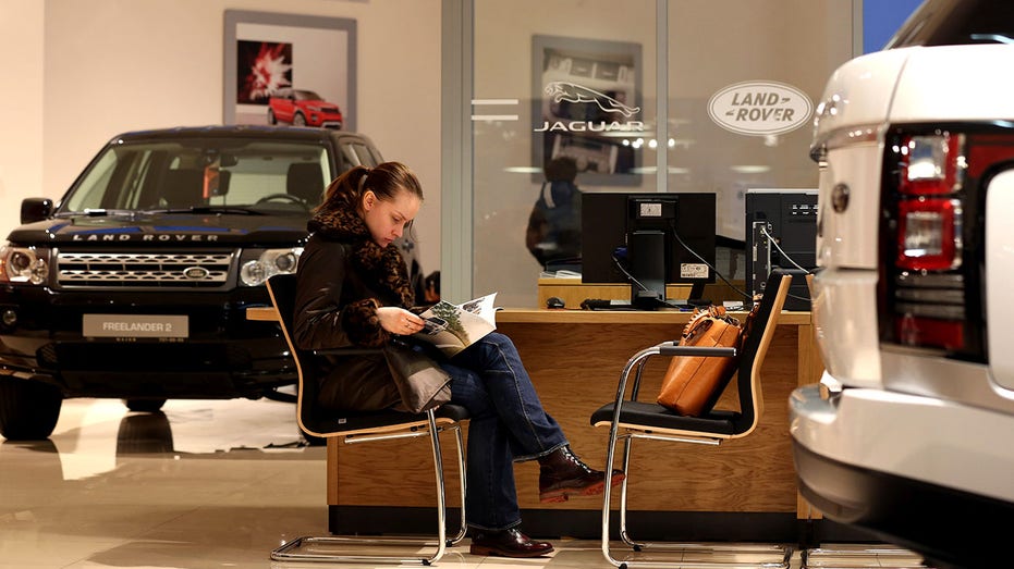 A customer sits and browses an automobile brochure inside a Jaguar Land Rover auto dealership