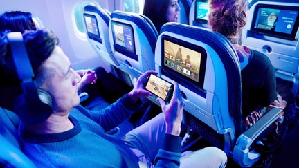A man games on a smartphone at the same time his seatback screen is illuminated with entertainment options. United Airlines did not share where or when this photo was taken.  - Fox Business News
