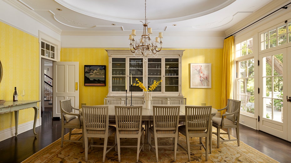 The dining room shows yellow walls and a big table sufficiently 10 guests.
