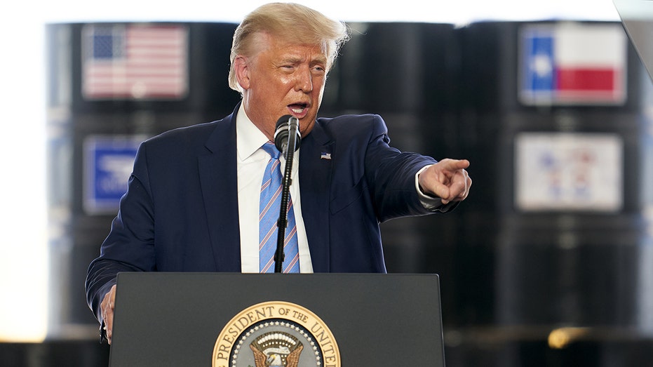 Donald Trump speaks on stage with oil barrels behind him