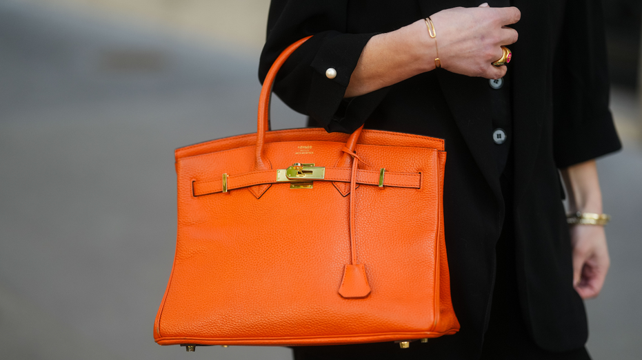 A woman carries an orange Hermes Birkin bag