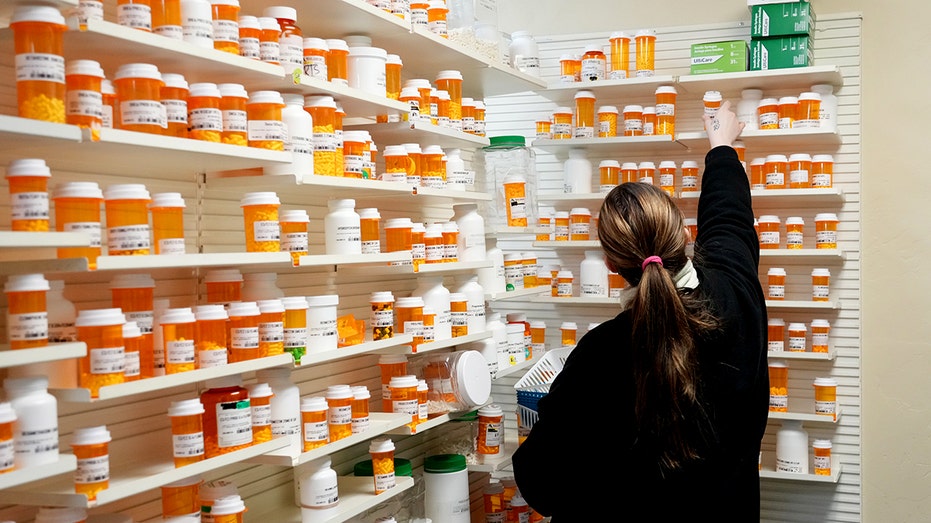 A pharmacy tech pulls medication from a shelf inside a pharmacy.