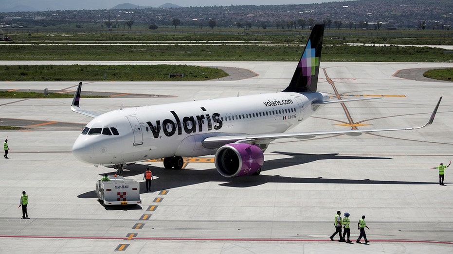 Airport workers stand near Volaris airplane as it is parked on tarmac