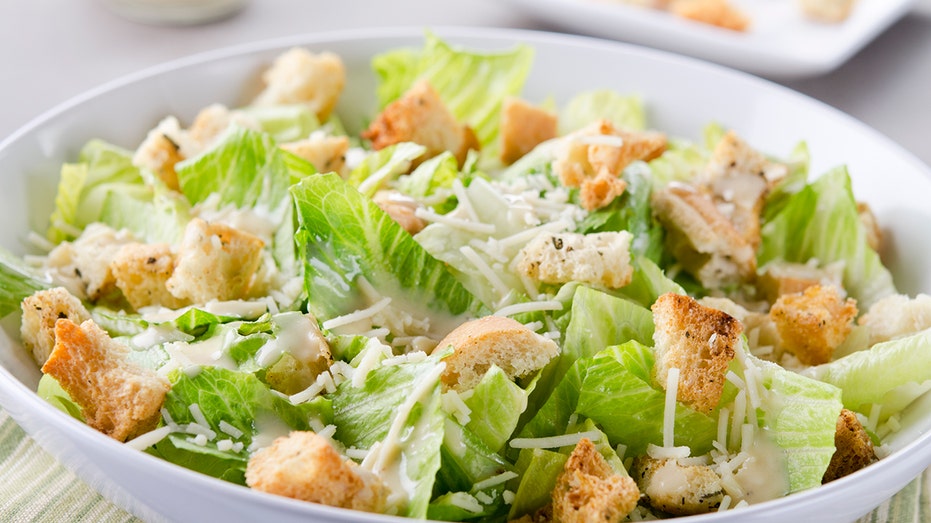 A bowl of Caesar Salad with croutons and cheese on table