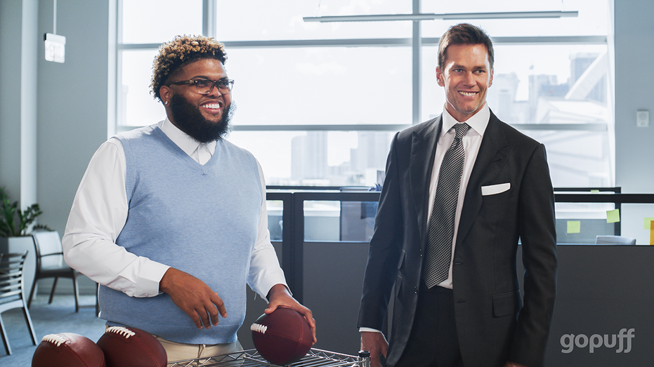 Tom Brady and Druski look on with footballs