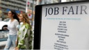 A job fair sign as people walk by in the background.