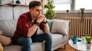A young man sits on a couch inside a home. - Fox Business News