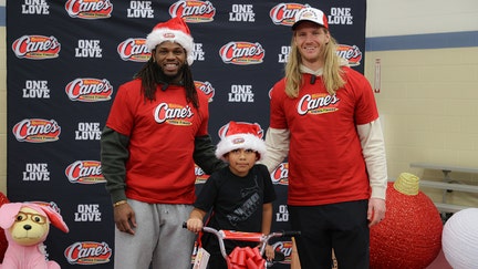 Josh Metellus and Andrew Van Ginkel poses with child at Raising Cane's bike giveaway. - Fox Business News