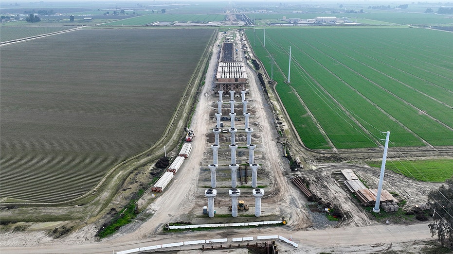 Construction crews and equipment work along an elevated rail structure under construction in California’s Central Valley.