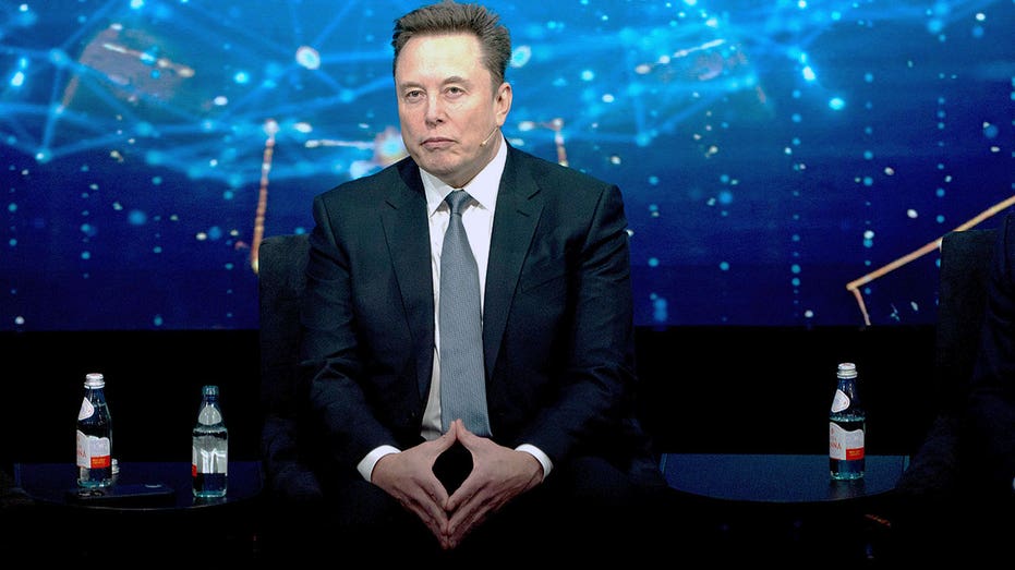 Elon Musk sits in a suit during a panel discussion in Washington, D.C.