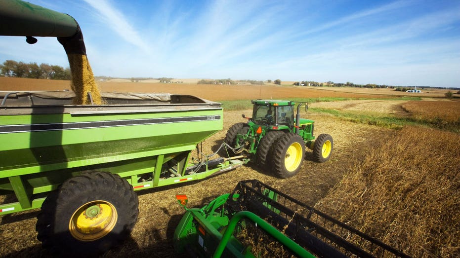 A John Deere tractor pulls a container as a combine harvests soybeans.