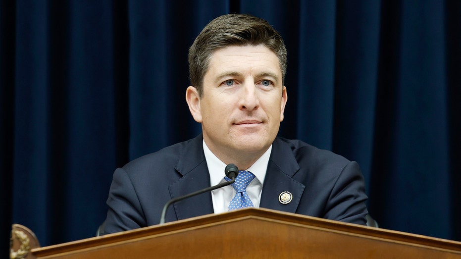 A congressman speaks into a microphone during a formal hearing room session on Capitol Hill.
