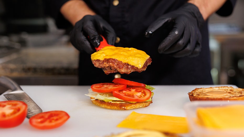 The cook in the kitchen prepares a cheeseburger and puts a cutlet with melted cheese.